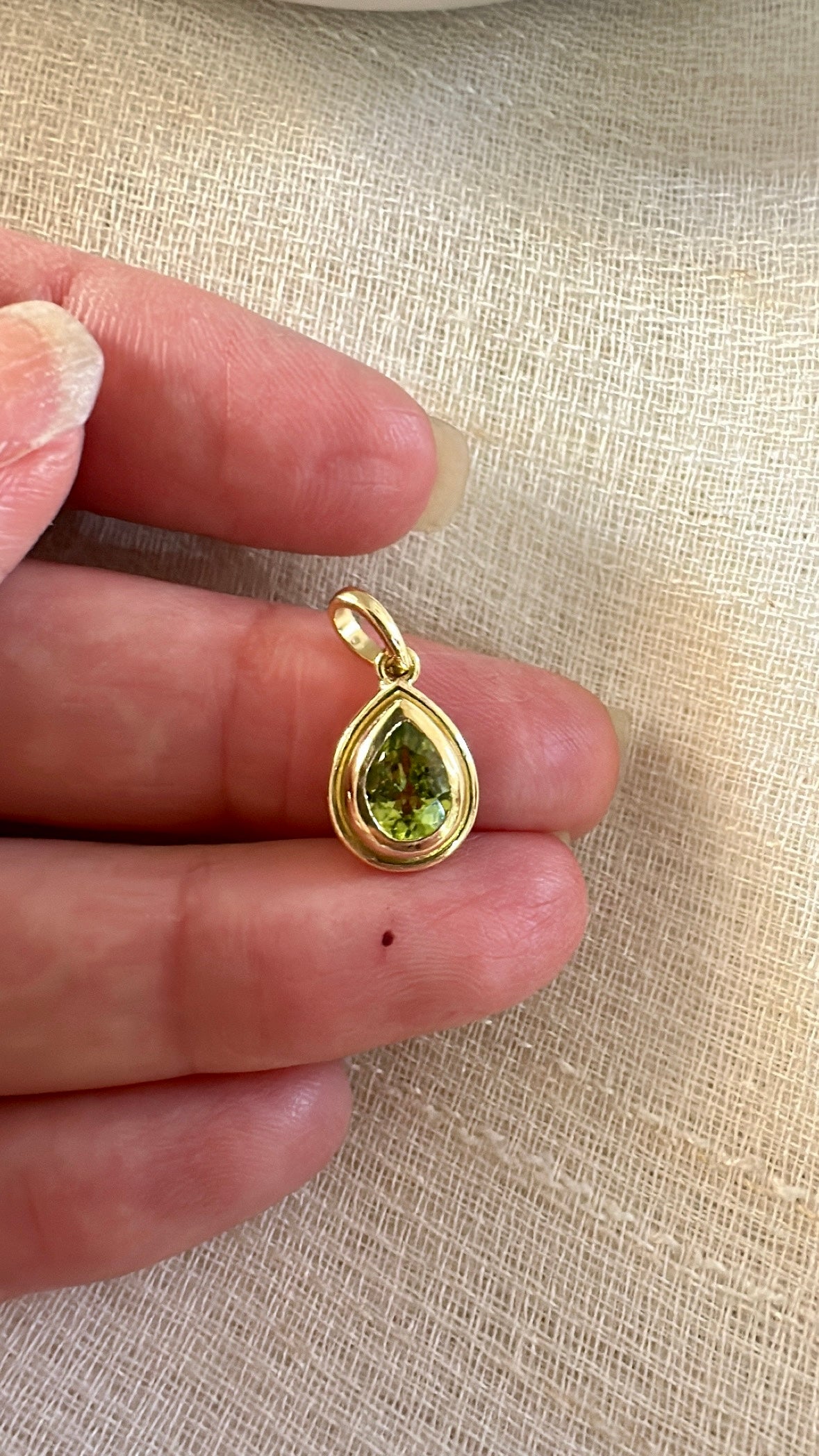Pear shaped peridot pendant with a solid gold back and an opening behind the stone