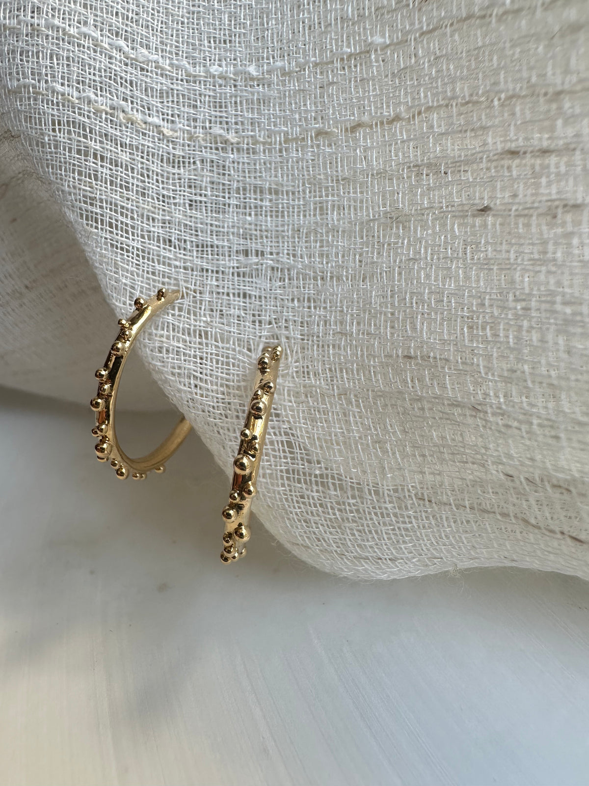 Medium gold hoop earrings with intricate granules along the top