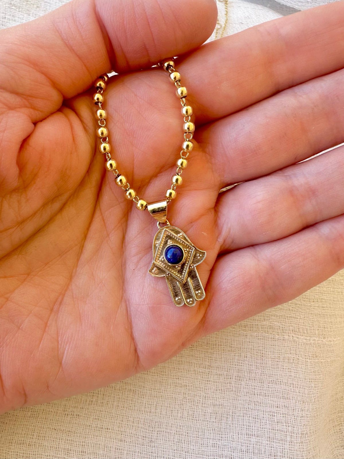 Hamsa hand pendant with a 4mm lapis lazuli cabochon in yellow gold