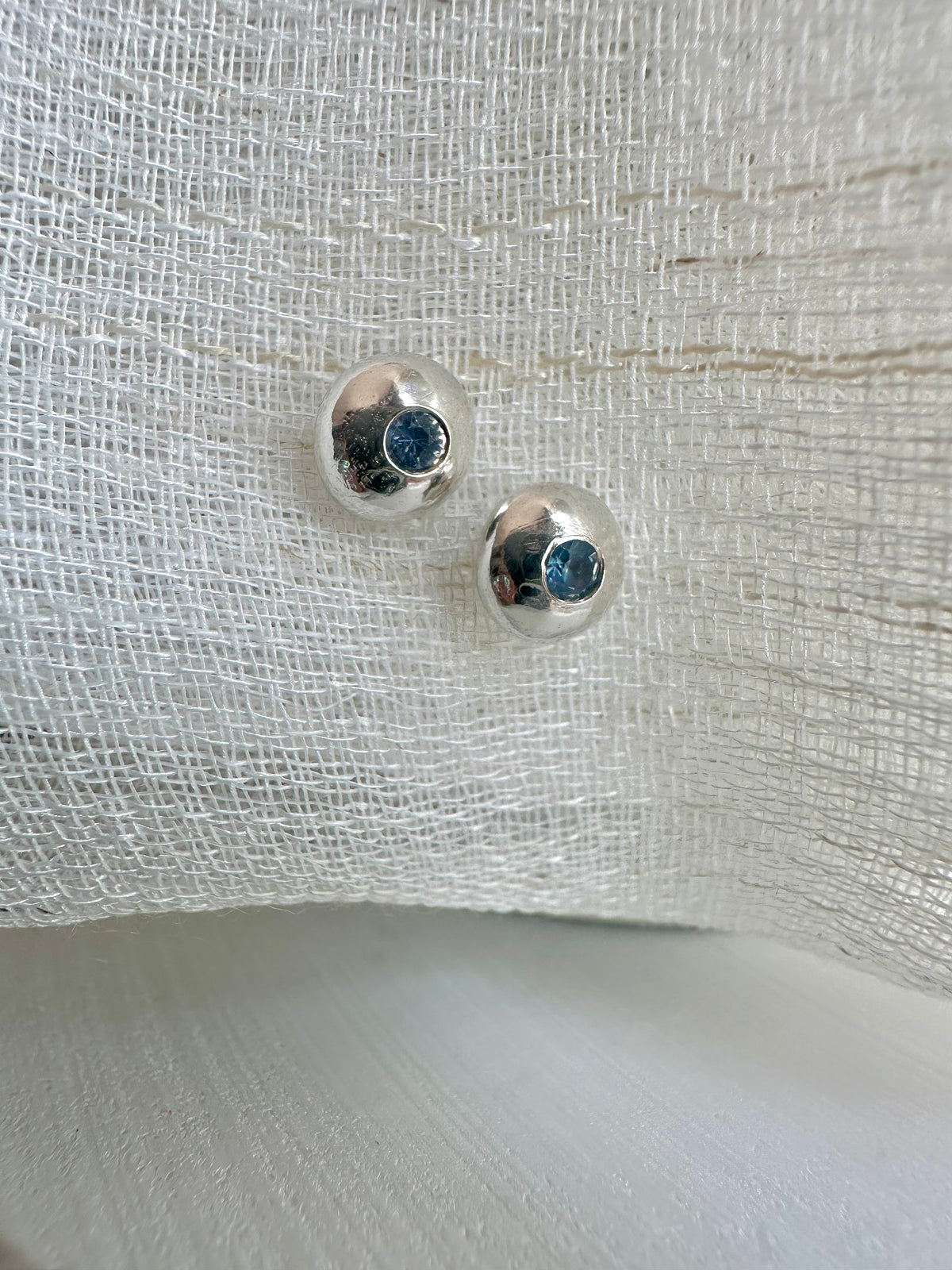 Light to mid blue sapphire set flush in a silver button stud