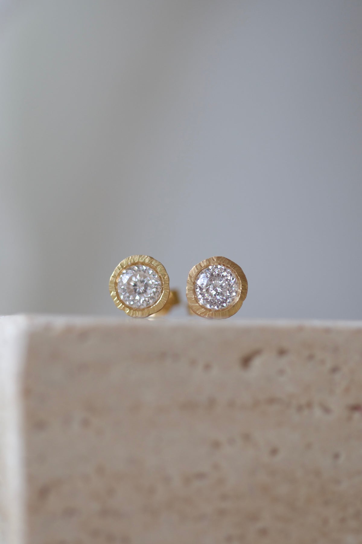 Pair of Glypto gold diamond studs on a travertine stone block