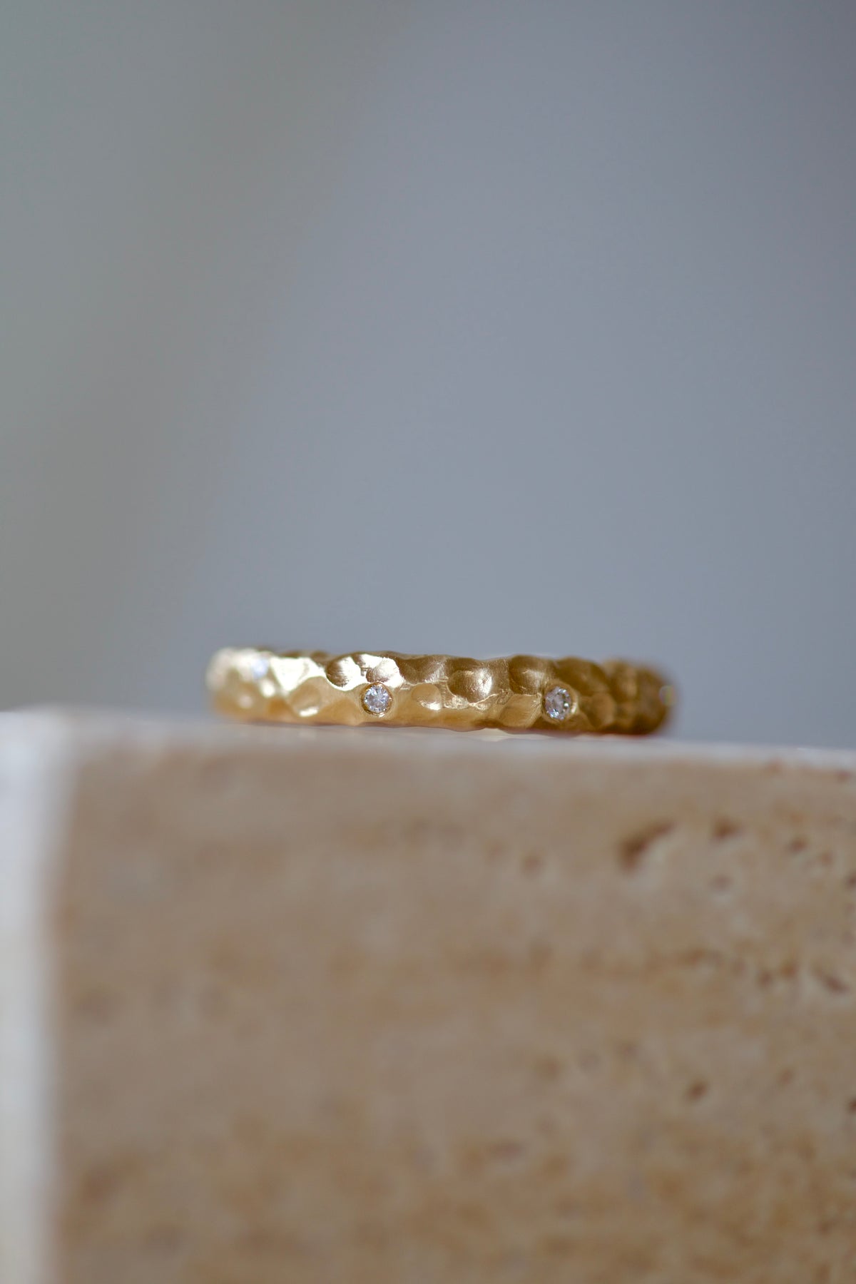 Glypto Diamond Band on a travertine stone block, small diamonds set flush in the hammered gold