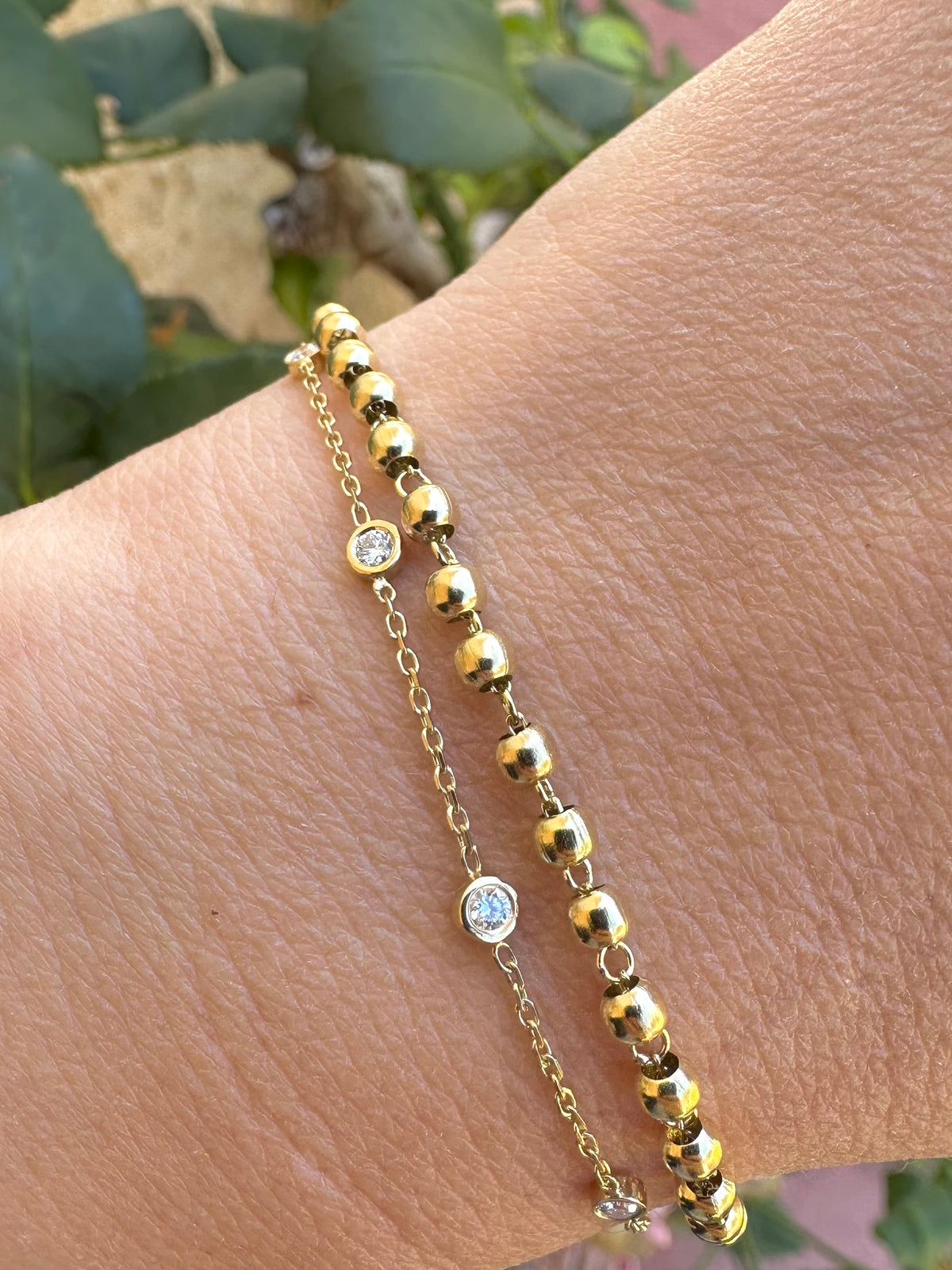 Stacked 18K solid gold bracelets with a gold bead bracelet and a lab diamond station bracelet