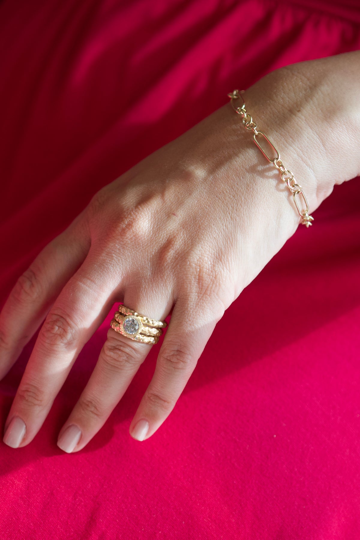 Glypto Solitaire Ring worn with two hammered bands, hand resting on a red surface