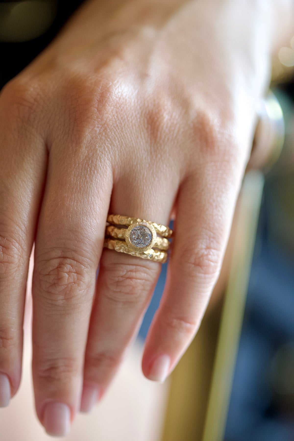 Glypto Solitaire Ring worn on a finger, stacked with two hammered gold bands