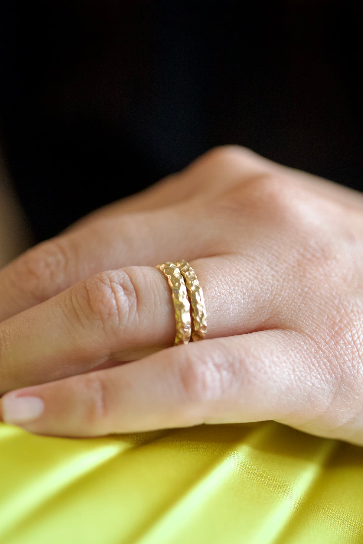 Two hammered gold bands stacked on a finger, one is the Glypto Diamond Band